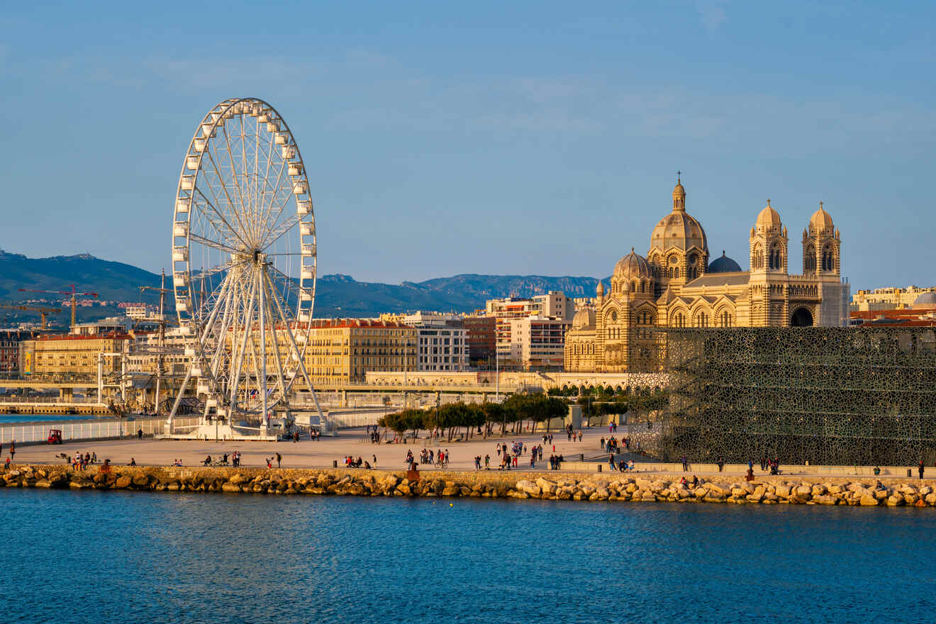 Sunset view over Marseille featuring the iconic Ferris wheel beside the ornate Cathedral of Notre-Dame de la Major, with the Mediterranean Sea in the background